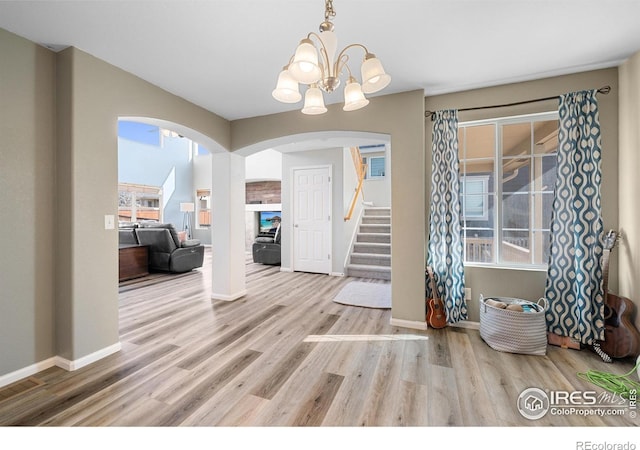 entrance foyer with arched walkways, stairway, a notable chandelier, and wood finished floors