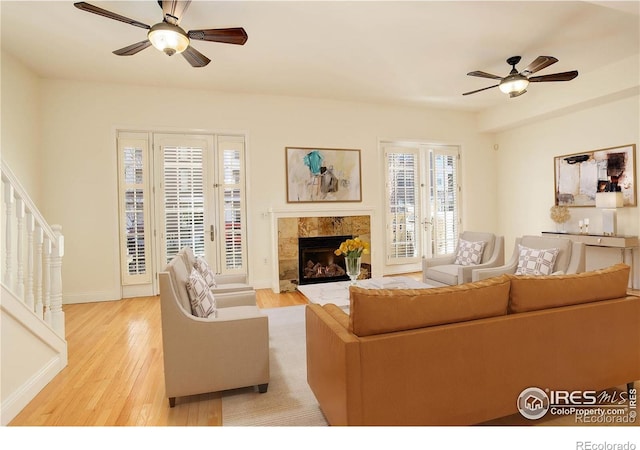 living room featuring light wood-style flooring, a fireplace, a ceiling fan, and stairs