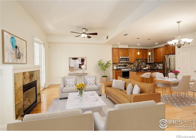 living area with visible vents, a fireplace, light wood-style floors, and ceiling fan with notable chandelier