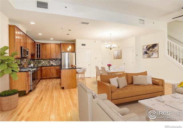 living room with visible vents, an inviting chandelier, light wood-style floors, and stairs