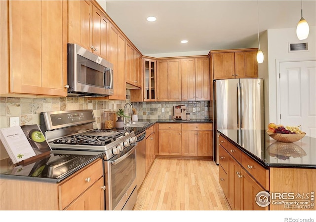 kitchen featuring glass insert cabinets, light wood-style flooring, dark stone counters, stainless steel appliances, and a sink