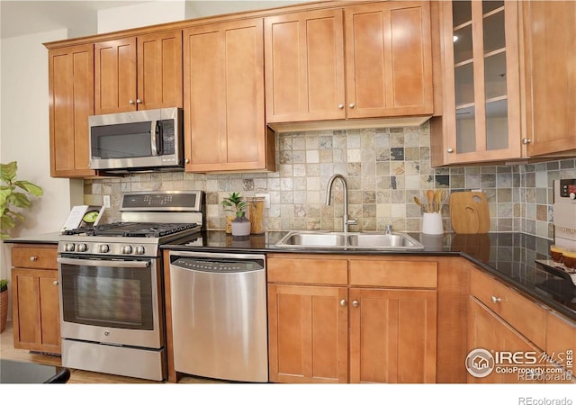 kitchen featuring tasteful backsplash, glass insert cabinets, a sink, appliances with stainless steel finishes, and brown cabinetry
