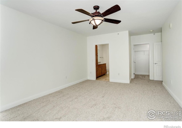 unfurnished bedroom with light carpet, a walk in closet, ensuite bath, and baseboards