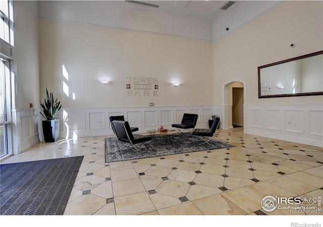 living area featuring arched walkways, a high ceiling, light tile patterned floors, and a decorative wall