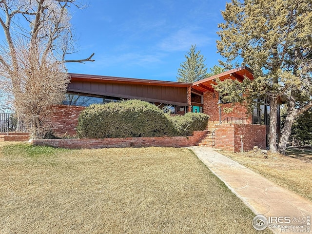 view of front of house featuring board and batten siding, a front lawn, and brick siding