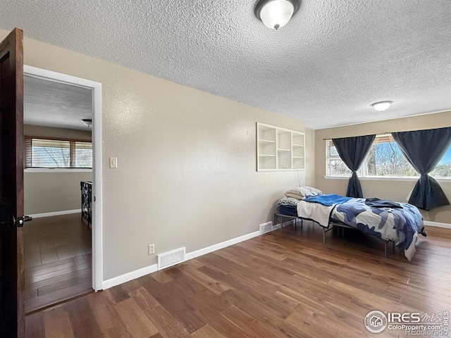 bedroom with visible vents, baseboards, wood finished floors, and a textured ceiling