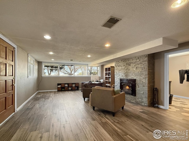living room featuring wood finished floors, a textured ceiling, a stone fireplace, and visible vents