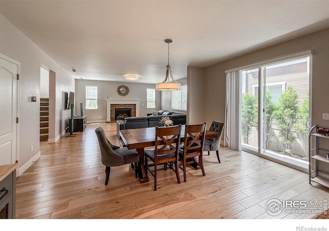 dining space with a fireplace with raised hearth, light wood finished floors, baseboards, and stairway