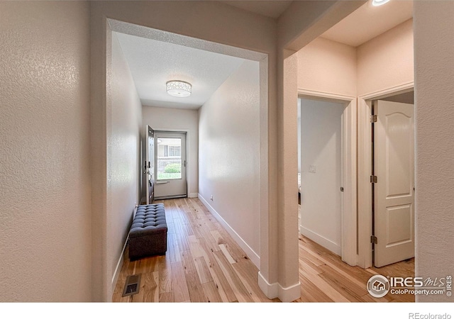 doorway to outside featuring light wood finished floors, a textured wall, and baseboards