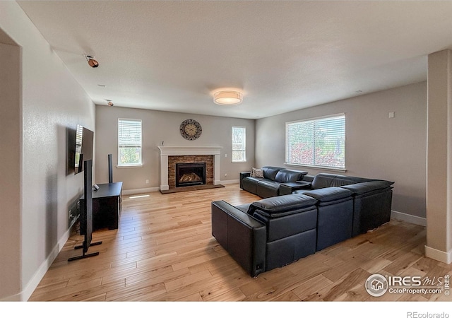 living area with light wood-style flooring, baseboards, and a stone fireplace
