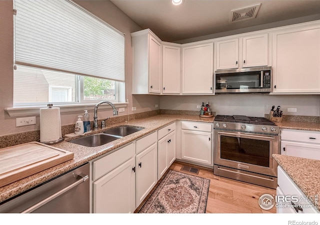 kitchen with stainless steel appliances, a sink, white cabinets, light wood-style floors, and recessed lighting
