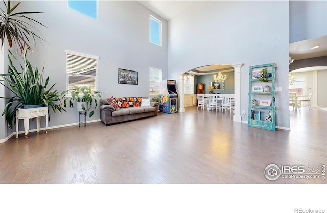 living area with arched walkways, a towering ceiling, a chandelier, decorative columns, and wood finished floors