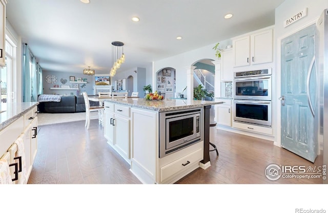 kitchen with stainless steel appliances, arched walkways, wood finished floors, open floor plan, and recessed lighting