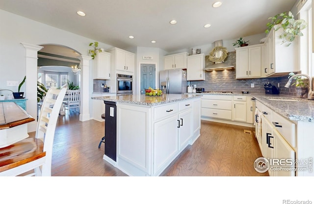kitchen with appliances with stainless steel finishes, a sink, ornate columns, arched walkways, and light wood-style floors