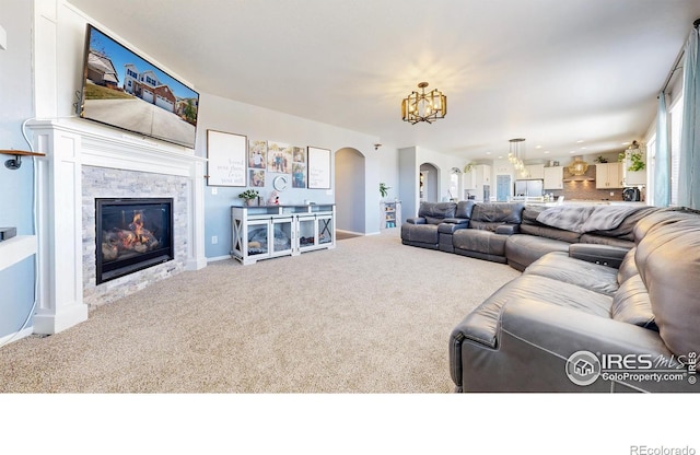 carpeted living room with arched walkways, a chandelier, a stone fireplace, and baseboards