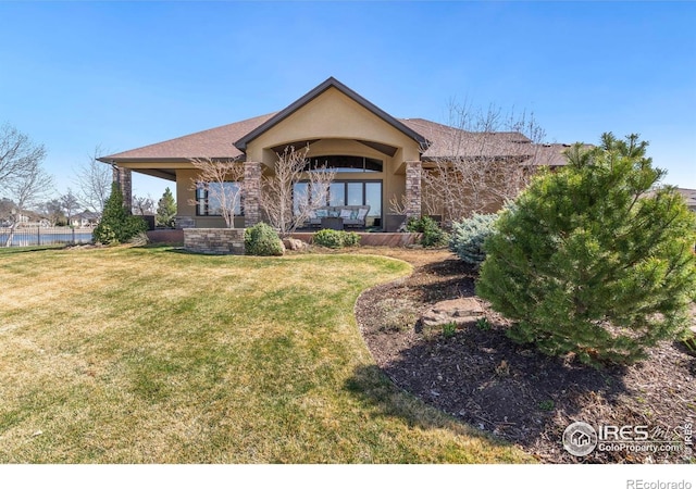 back of property with a yard, roof with shingles, stucco siding, and stone siding