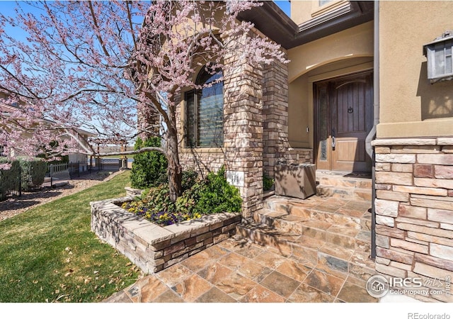 view of exterior entry featuring a yard, stucco siding, and fence
