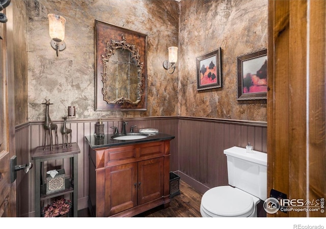 half bath with vanity, wainscoting, toilet, and wood finished floors