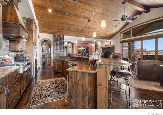 kitchen with a breakfast bar, premium range hood, ceiling fan, stainless steel appliances, and wooden ceiling