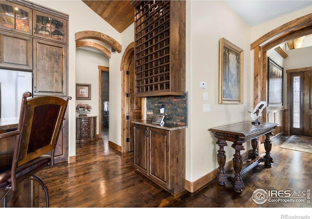 wine area featuring dark wood-type flooring, baseboards, arched walkways, and lofted ceiling