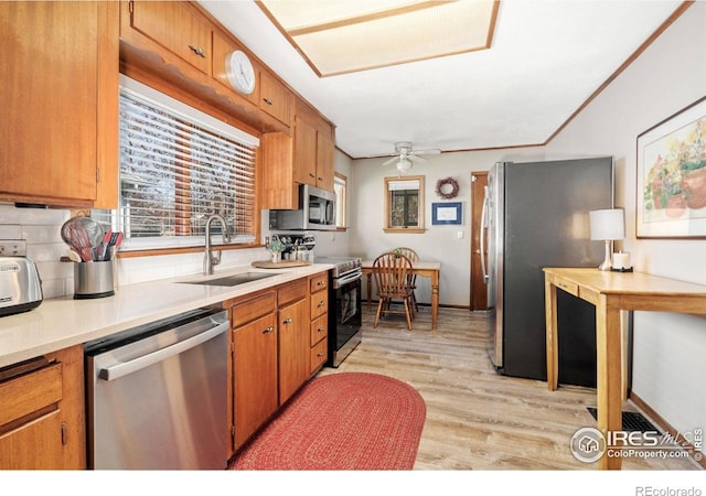 kitchen featuring light wood-style flooring, a sink, light countertops, stainless steel appliances, and brown cabinets