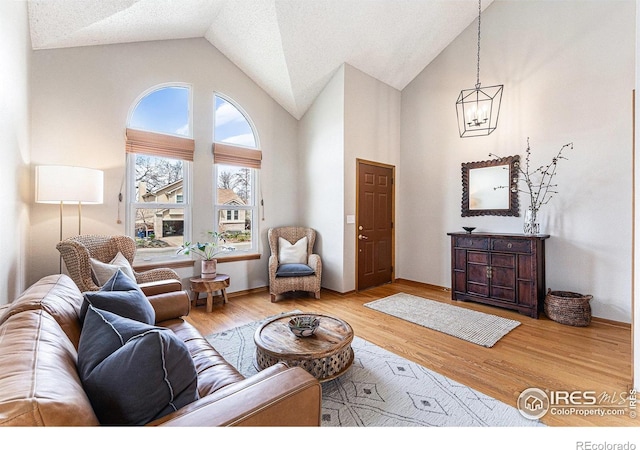 living area with wood finished floors, high vaulted ceiling, and an inviting chandelier