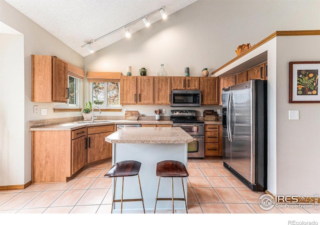 kitchen featuring rail lighting, light countertops, a kitchen island, stainless steel appliances, and a sink