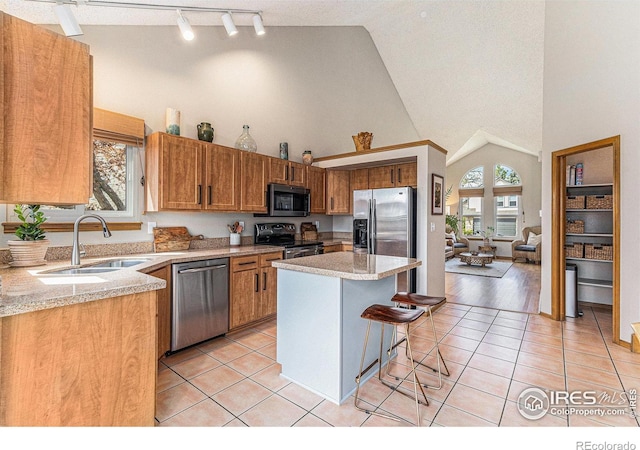 kitchen featuring high vaulted ceiling, appliances with stainless steel finishes, light countertops, a sink, and a breakfast bar area