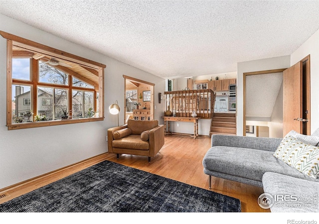 living room with a textured ceiling, wood finished floors, ceiling fan, and stairs