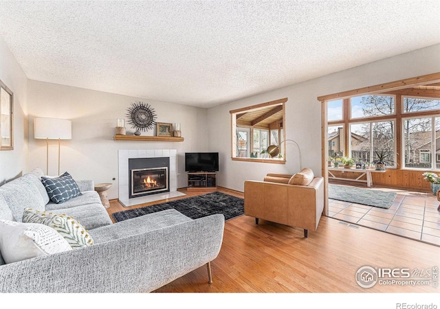 living area featuring a fireplace, visible vents, a textured ceiling, and wood finished floors