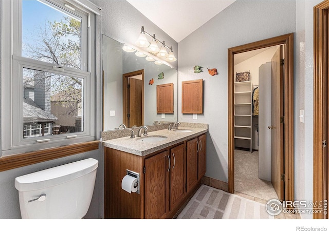 full bath with double vanity, a sink, vaulted ceiling, and toilet
