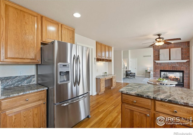 4748 Westbury Dr, Fort Collins, CO 80526 - kitchen featuring stainless steel fridge with ice dispenser, dark stone countertops, ceiling fan, light wood-type flooring, and a fireplace