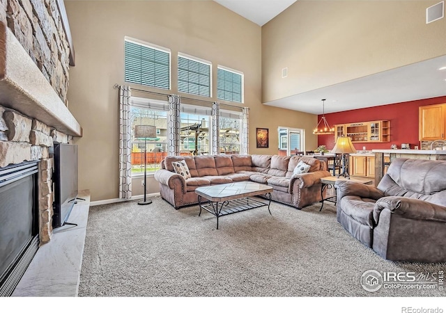 carpeted living area featuring a fireplace, a notable chandelier, a high ceiling, and visible vents