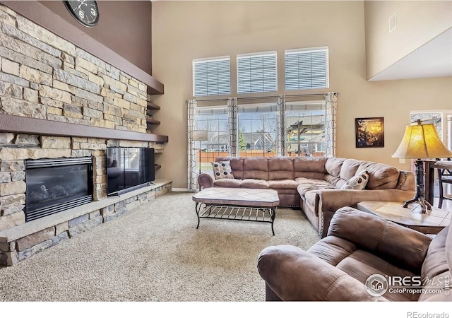 carpeted living room featuring a towering ceiling and a stone fireplace