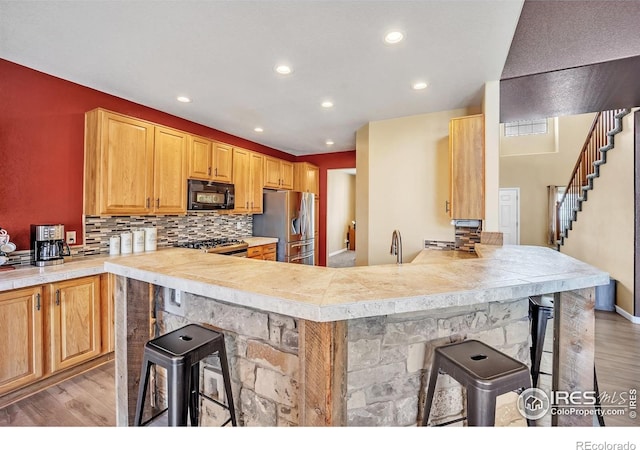 kitchen featuring light wood-type flooring, appliances with stainless steel finishes, a peninsula, and a breakfast bar