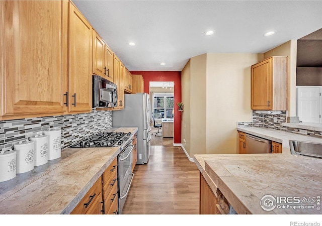 kitchen with tasteful backsplash, light wood-type flooring, baseboards, recessed lighting, and appliances with stainless steel finishes