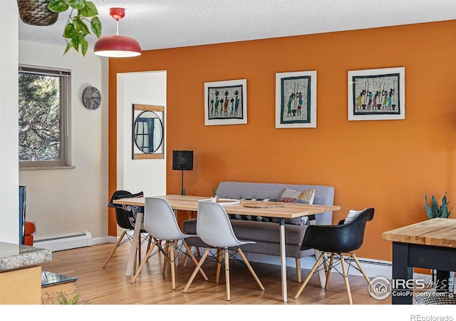 dining area featuring baseboards, a textured ceiling, wood finished floors, and baseboard heating