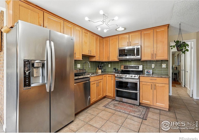 kitchen featuring light tile patterned floors, stone countertops, appliances with stainless steel finishes, a sink, and backsplash