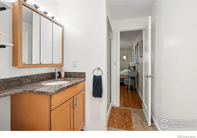 ensuite bathroom with tile patterned floors, vanity, baseboards, and connected bathroom