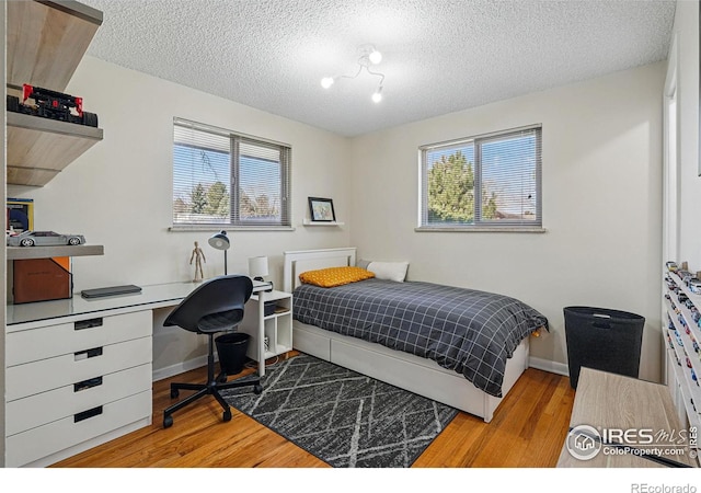 bedroom featuring a textured ceiling, wood finished floors, baseboards, and multiple windows