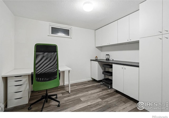 office featuring dark wood-type flooring, a textured ceiling, built in study area, and baseboards