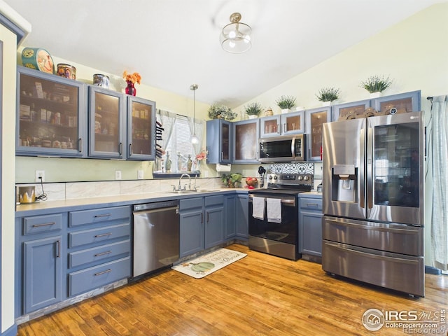 kitchen with a sink, wood finished floors, vaulted ceiling, pendant lighting, and stainless steel appliances