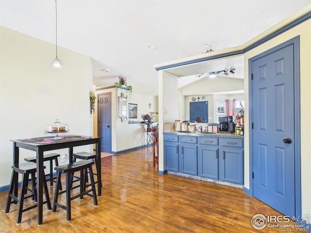 kitchen with baseboards, blue cabinetry, lofted ceiling, pendant lighting, and wood finished floors