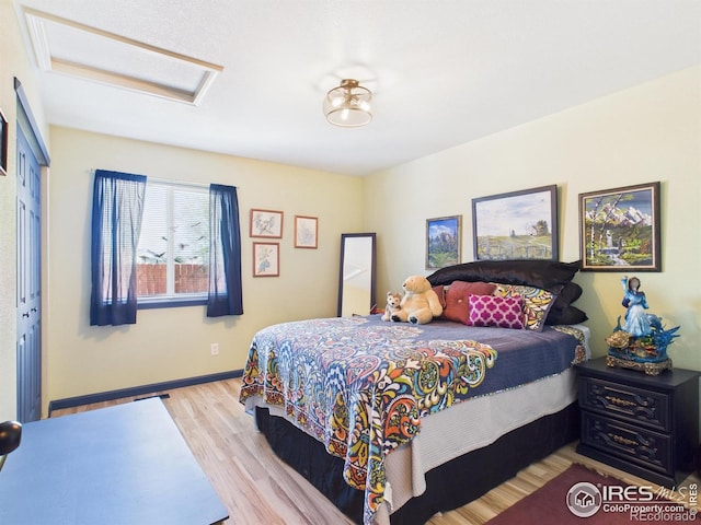 bedroom with wood finished floors, attic access, baseboards, and a closet