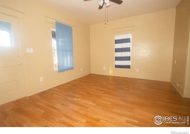 empty room featuring crown molding, light wood-style flooring, a ceiling fan, visible vents, and baseboards