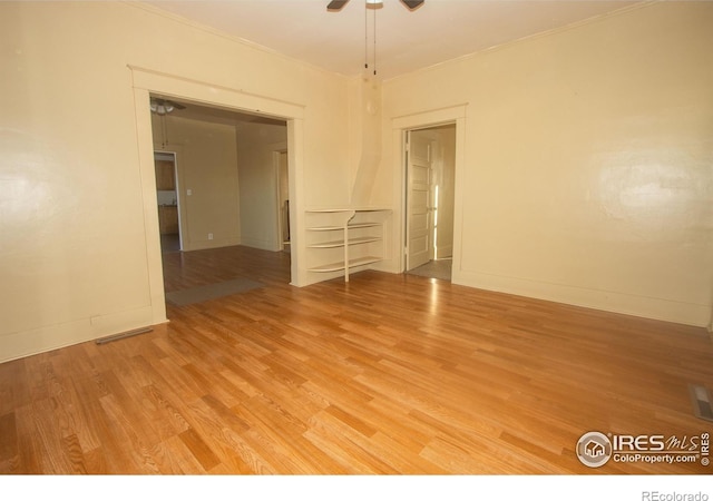 empty room with baseboards, light wood-type flooring, ornamental molding, a ceiling fan, and visible vents