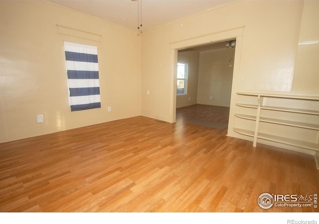 spare room featuring light wood-style flooring, baseboards, and crown molding
