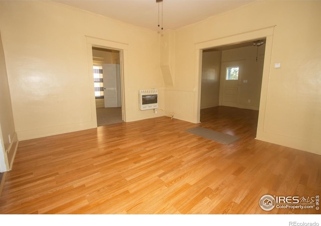 empty room with light wood-style flooring, baseboards, crown molding, and heating unit