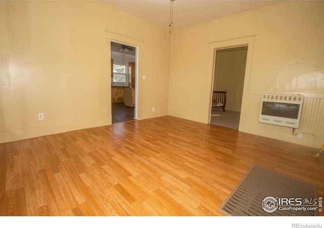 unfurnished living room with baseboards, ornamental molding, heating unit, and wood finished floors