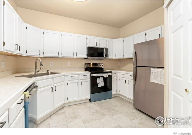 kitchen featuring a sink, tile counters, appliances with stainless steel finishes, and white cabinetry